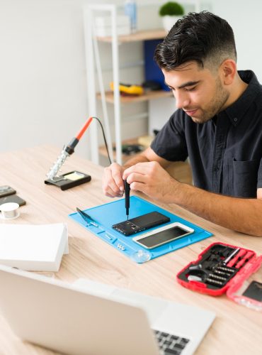 handsome-young-man-smiling-while-repairing-old-smartphone-male-technician-using-screwdriver-fix-broken-cellphone-workshop